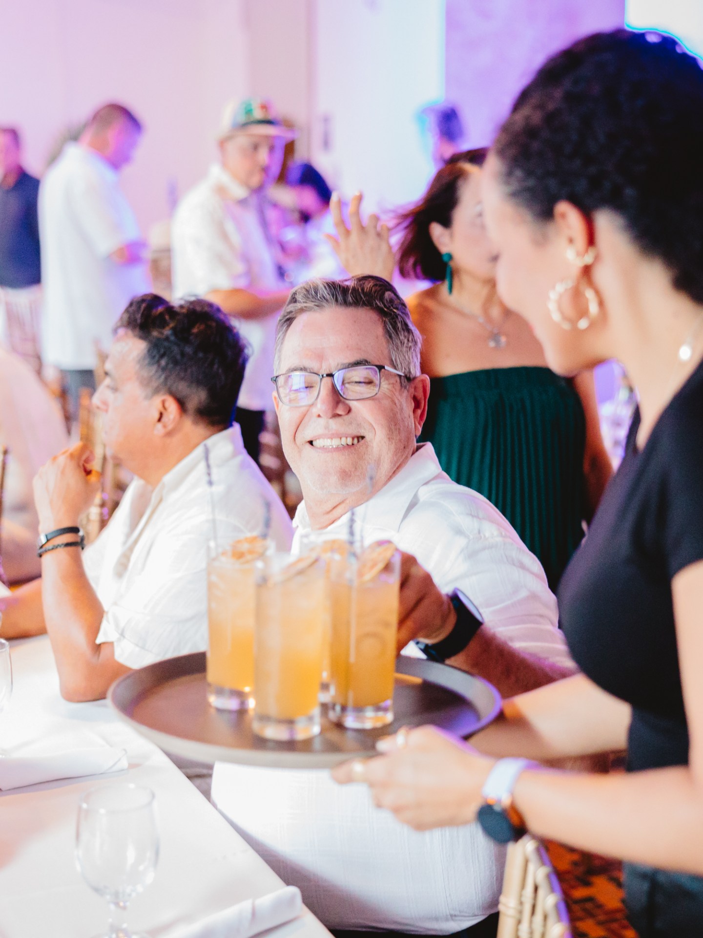 Smiling man receives drinks at a crowded indoor gathering.