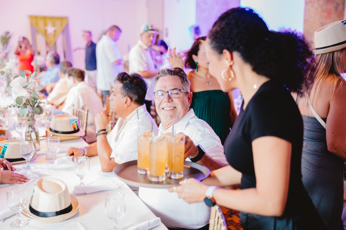 Gallery 2 Smiling man receives drinks at a crowded indoor gathering.