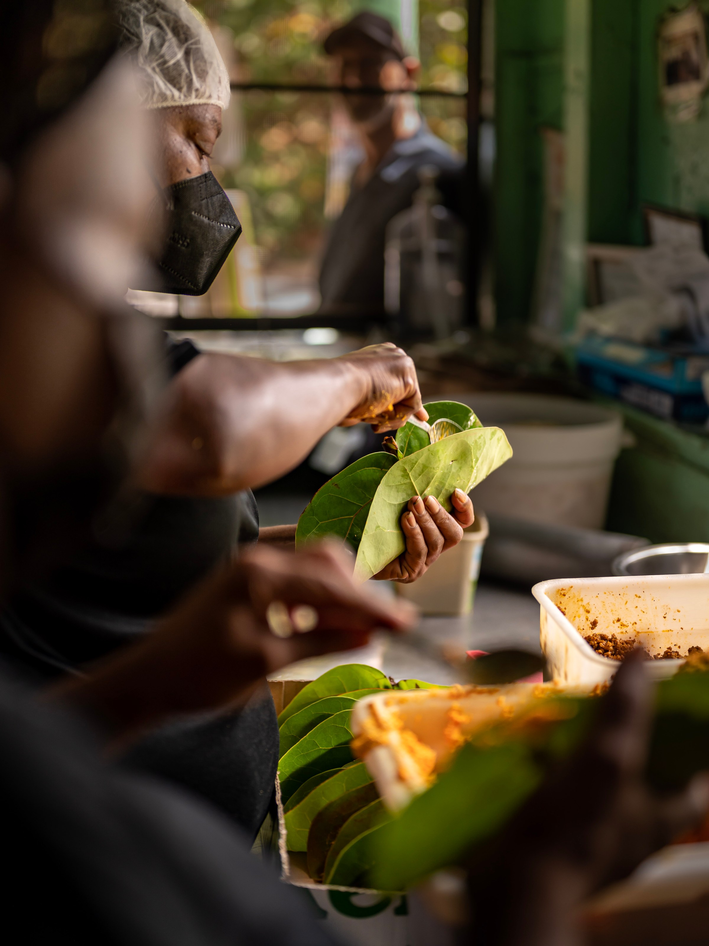 Person prepares food using large green leaves in a kitchen setting.