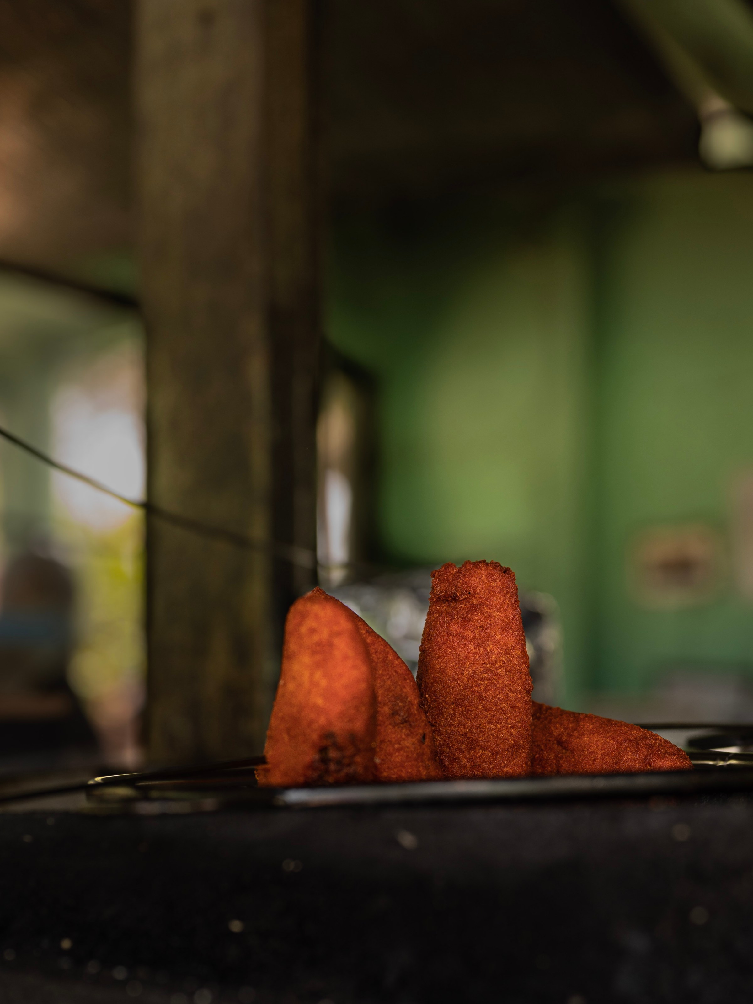 Close-up of three fried pastries on a tray in a dimly lit room.