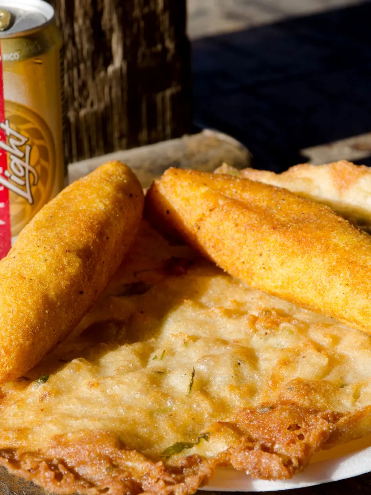 Two fried snacks with a beer can on a wooden table.