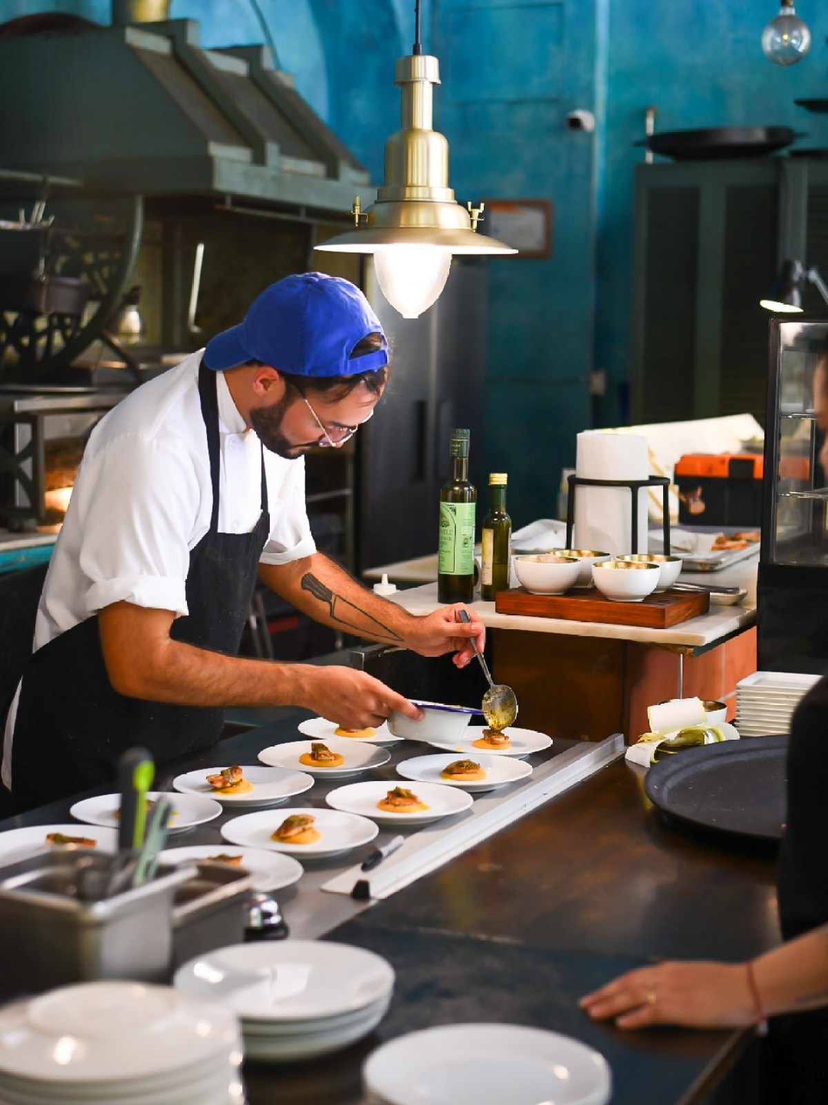 Chef in blue cap plating appetizers in a restaurant kitchen.