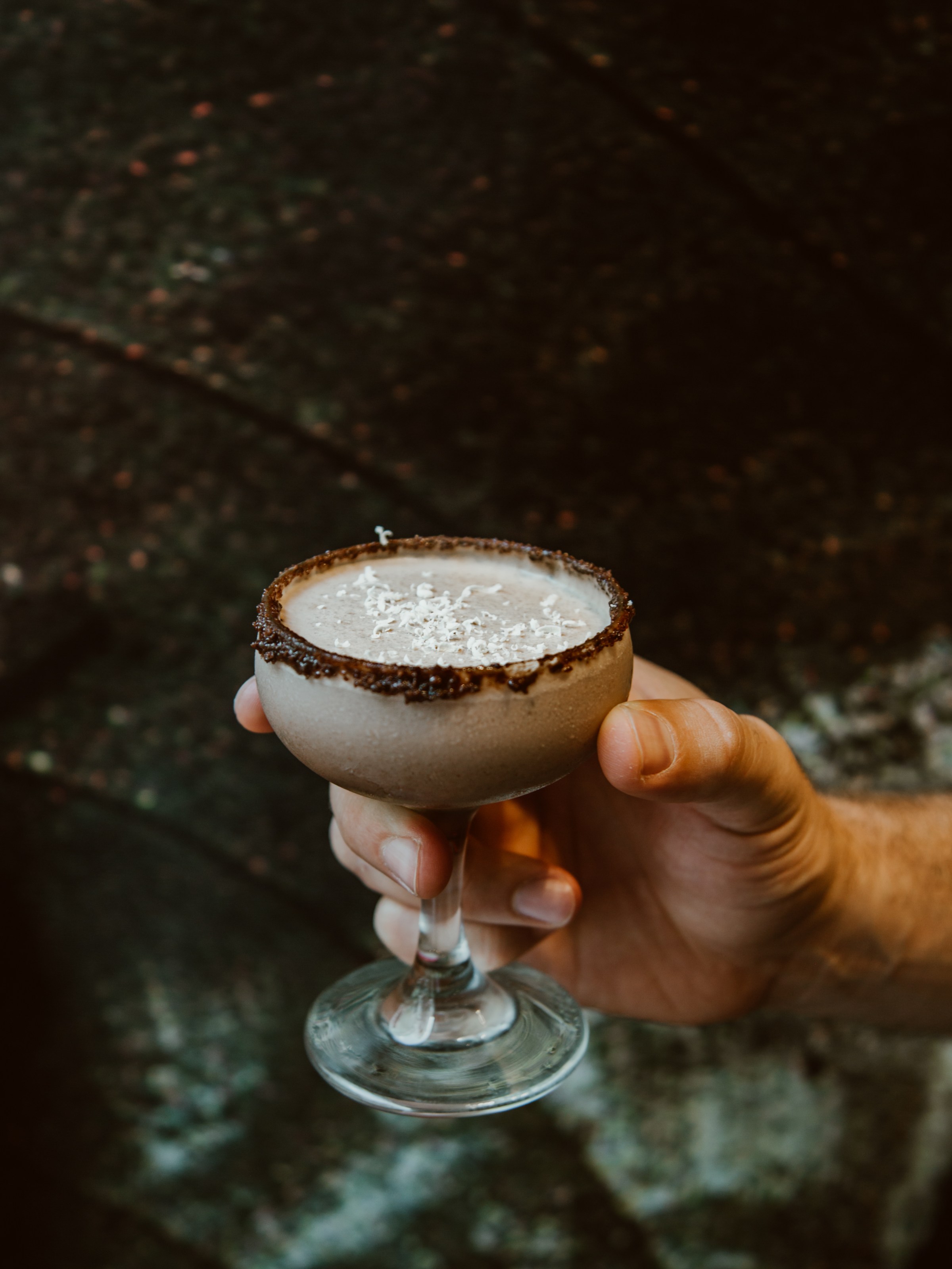 Hand holding a chocolate cocktail in a glass with grated white topping.
