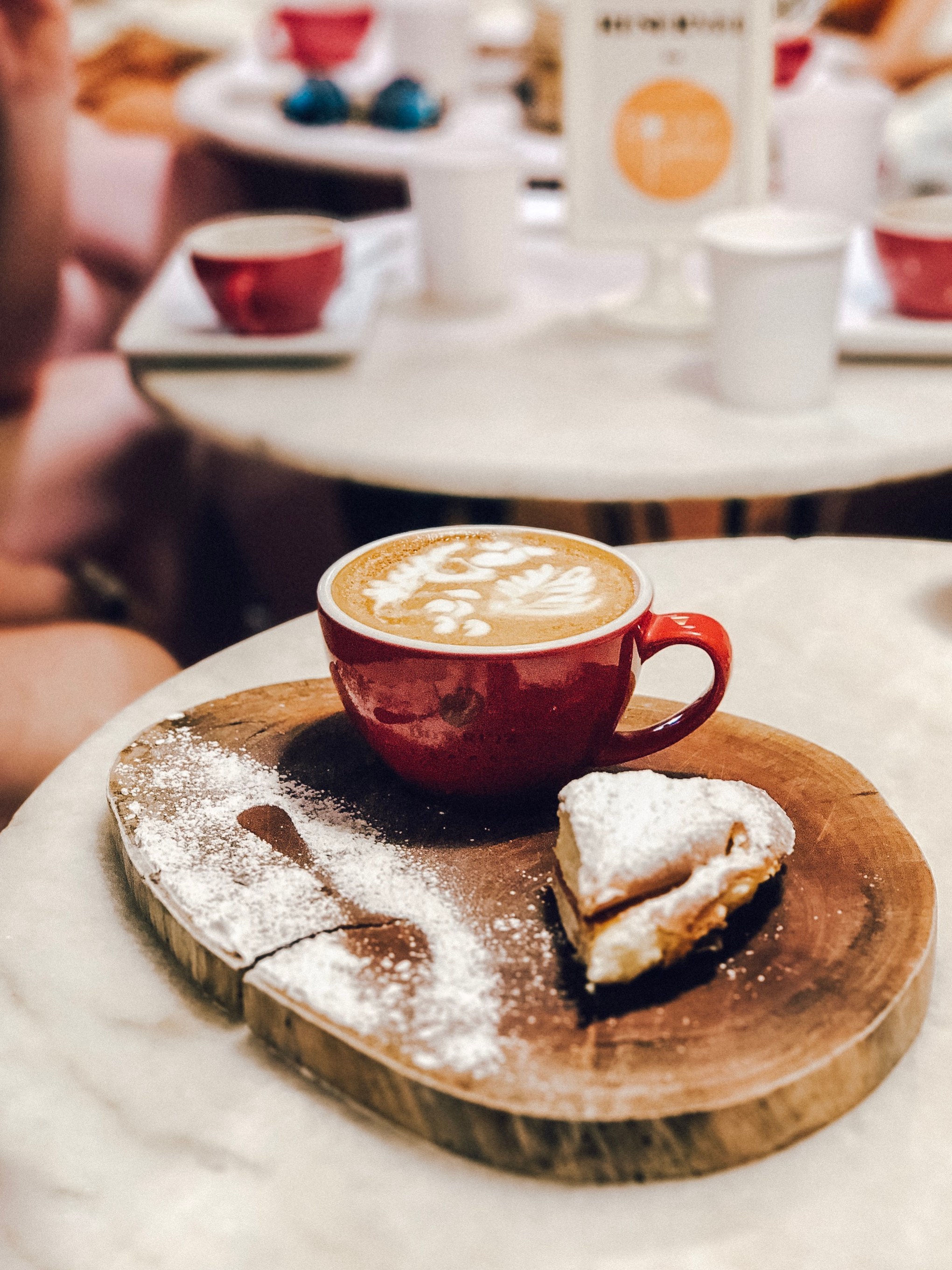 Latte art in red cup with pastry on wooden board on cafe table.