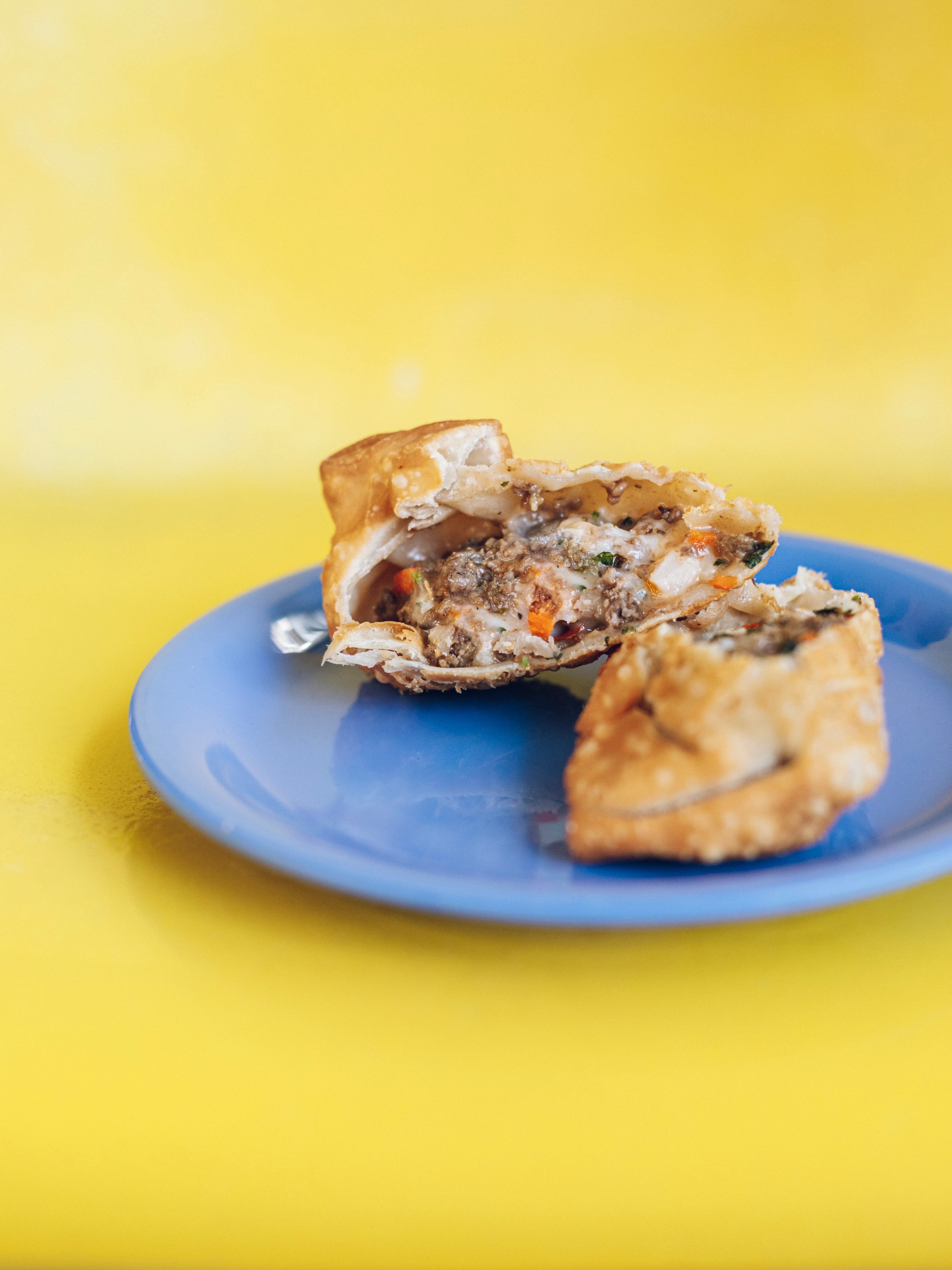 Sliced empanada on a blue plate against a yellow background.