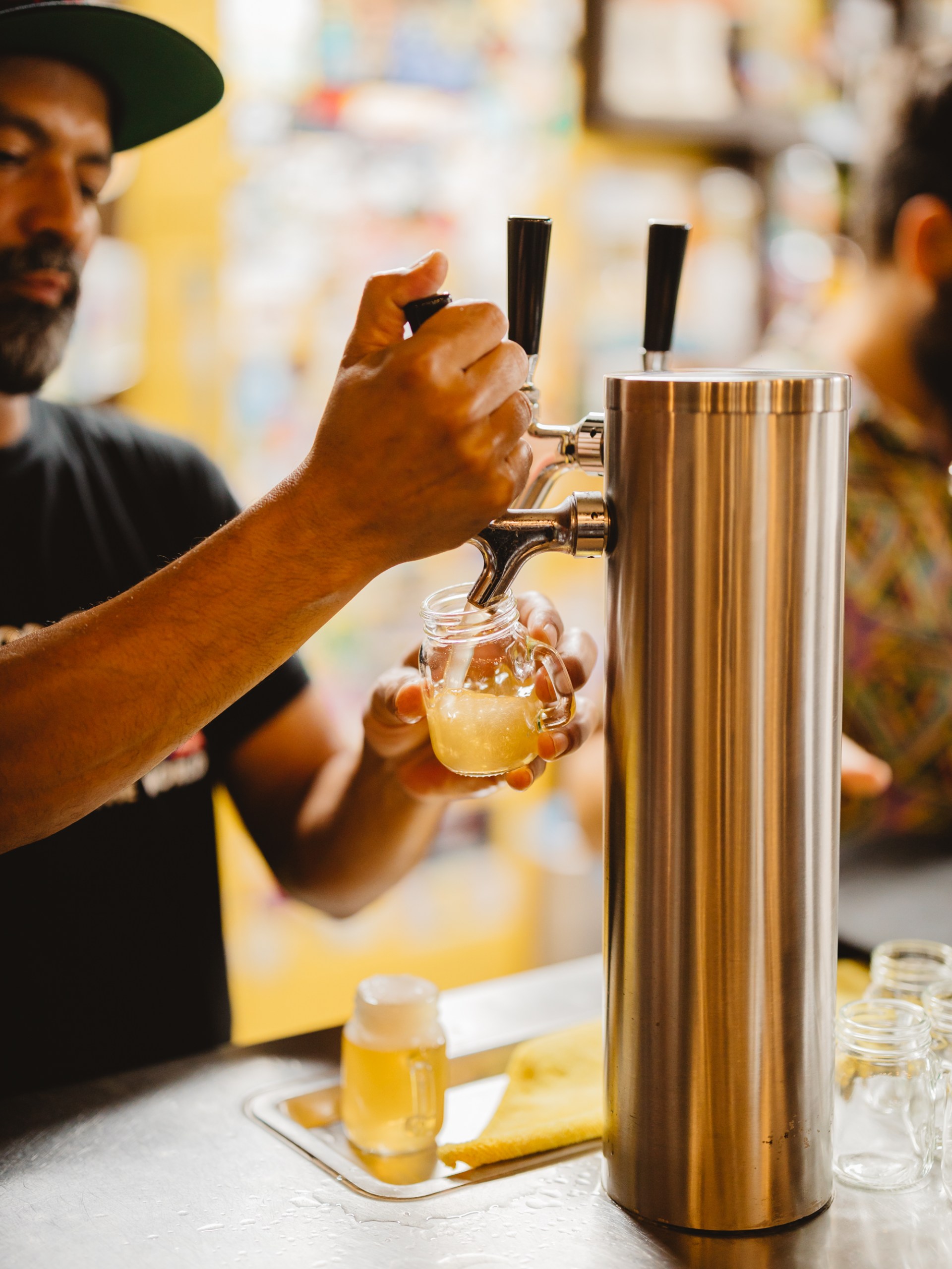 Person pouring draft beer into a small glass jar at a bar.