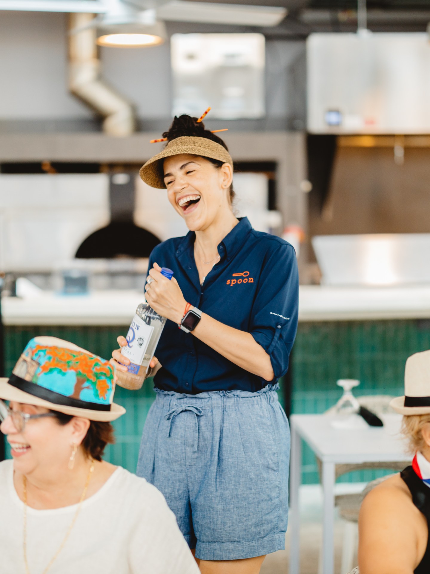 Smiling woman in visor serves drinks to seated diners in a casual restaurant.