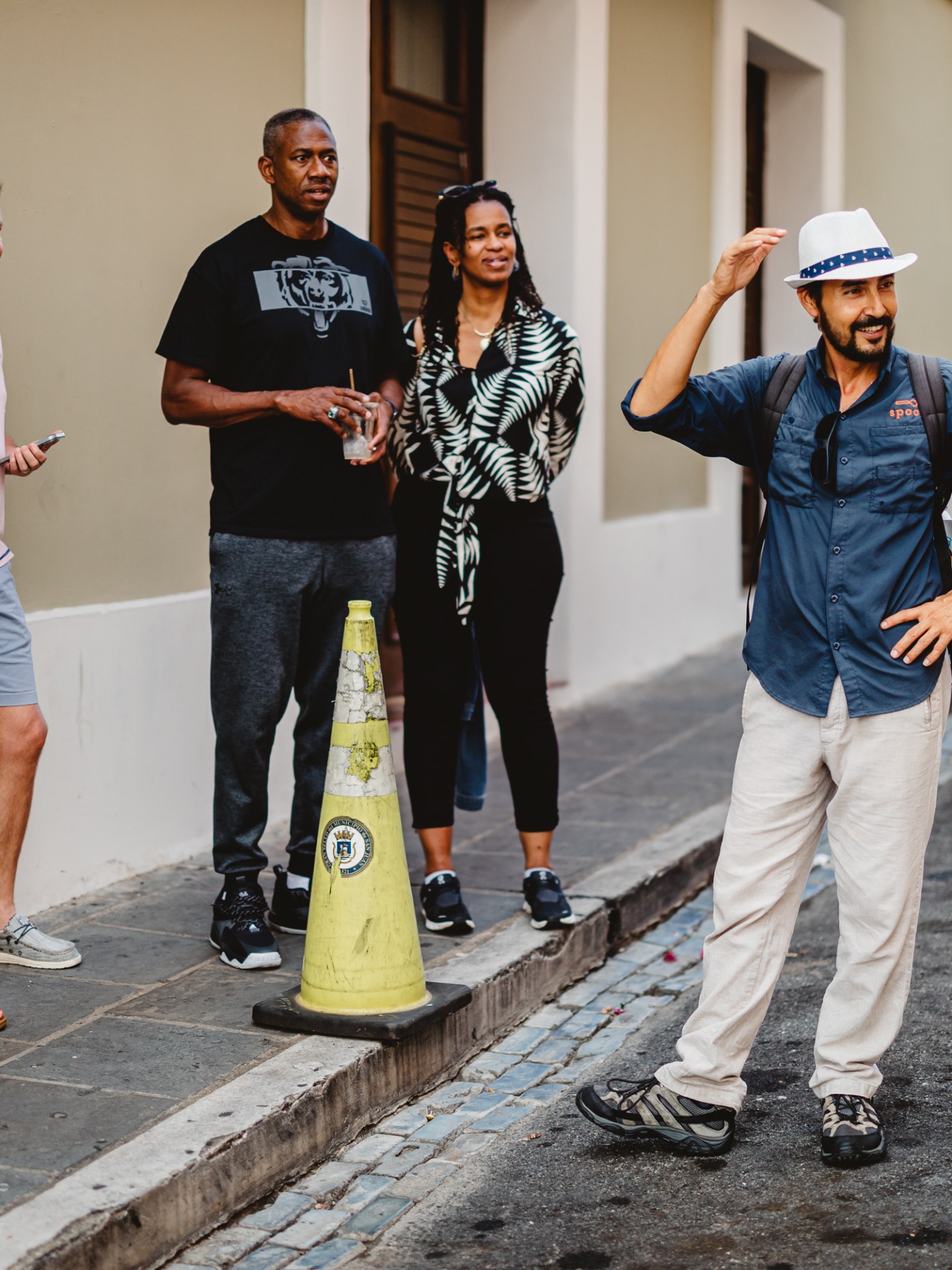 Tour guide talks to a group on a city street, gesturing with one hand on his hat.