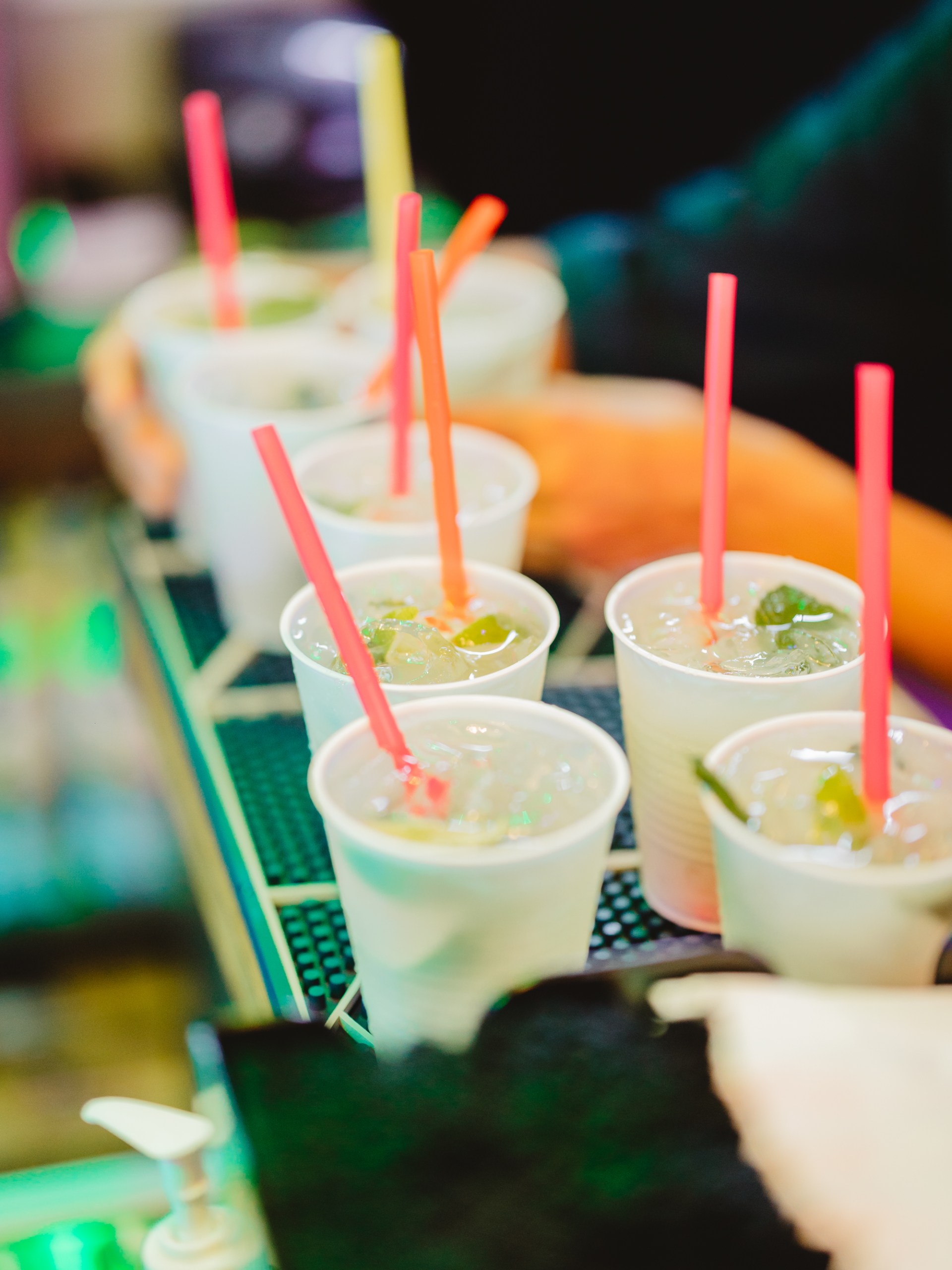 Row of plastic cups with ice and colorful straws on a bar counter.