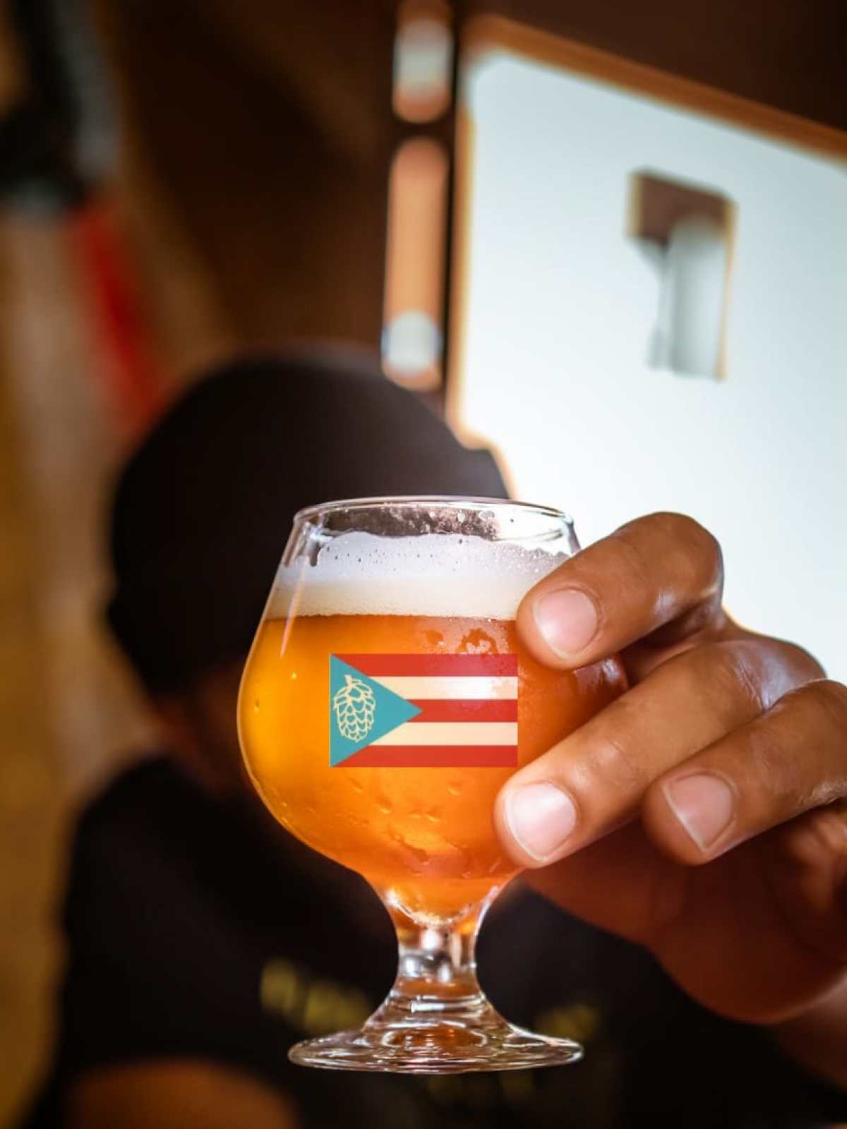 Person holding a glass of beer with a Puerto Rican flag design, background blurred.