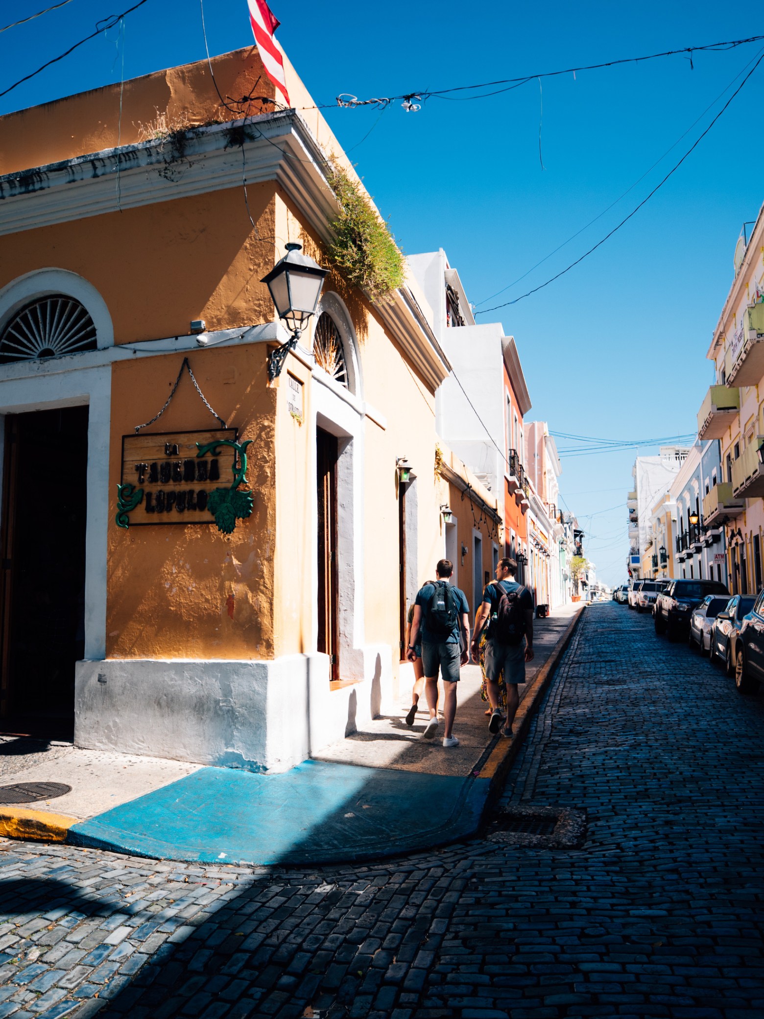 Colorful street scene with people walking by vibrant buildings under a clear blue sky.