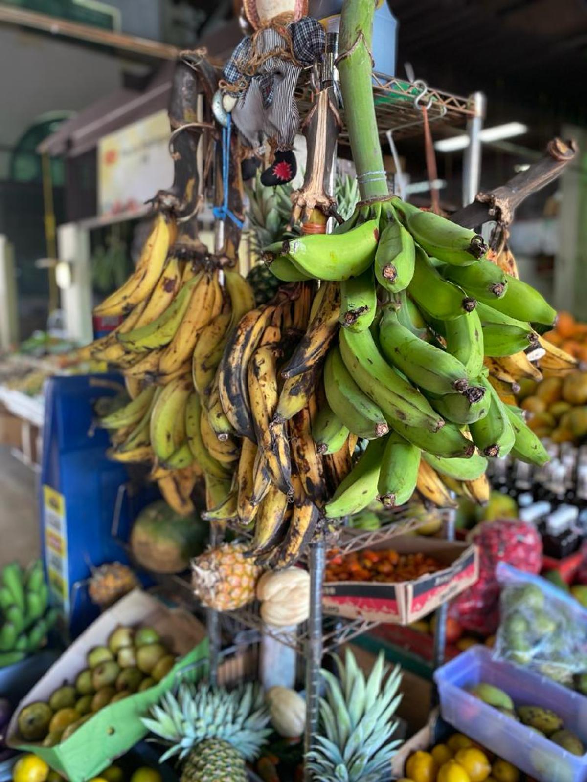 Bananas and pineapples on a crowded fruit market stand with various tropical fruits.