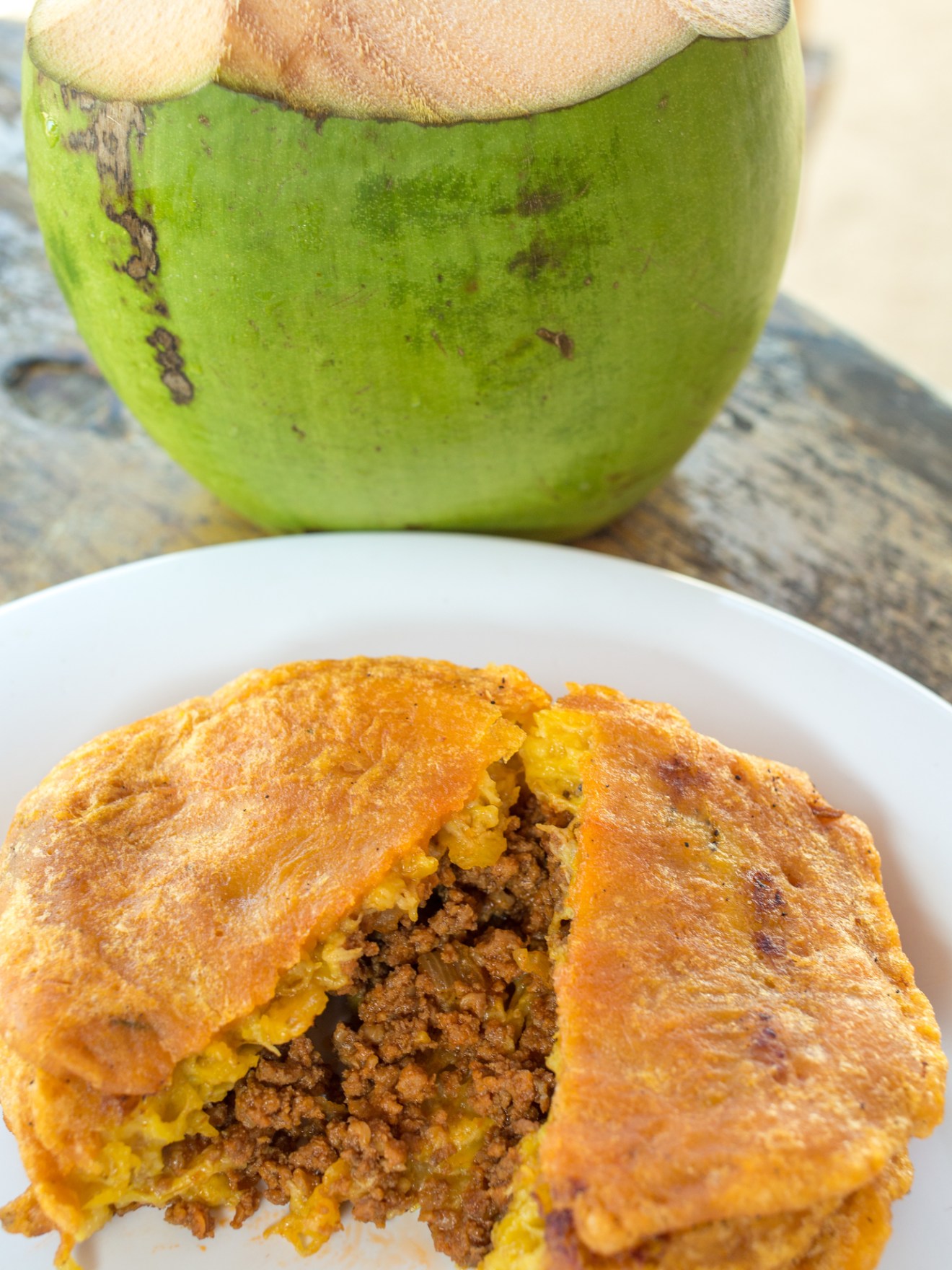 Arepa stuffed with meat on a white plate beside a green coconut with the top cut open.