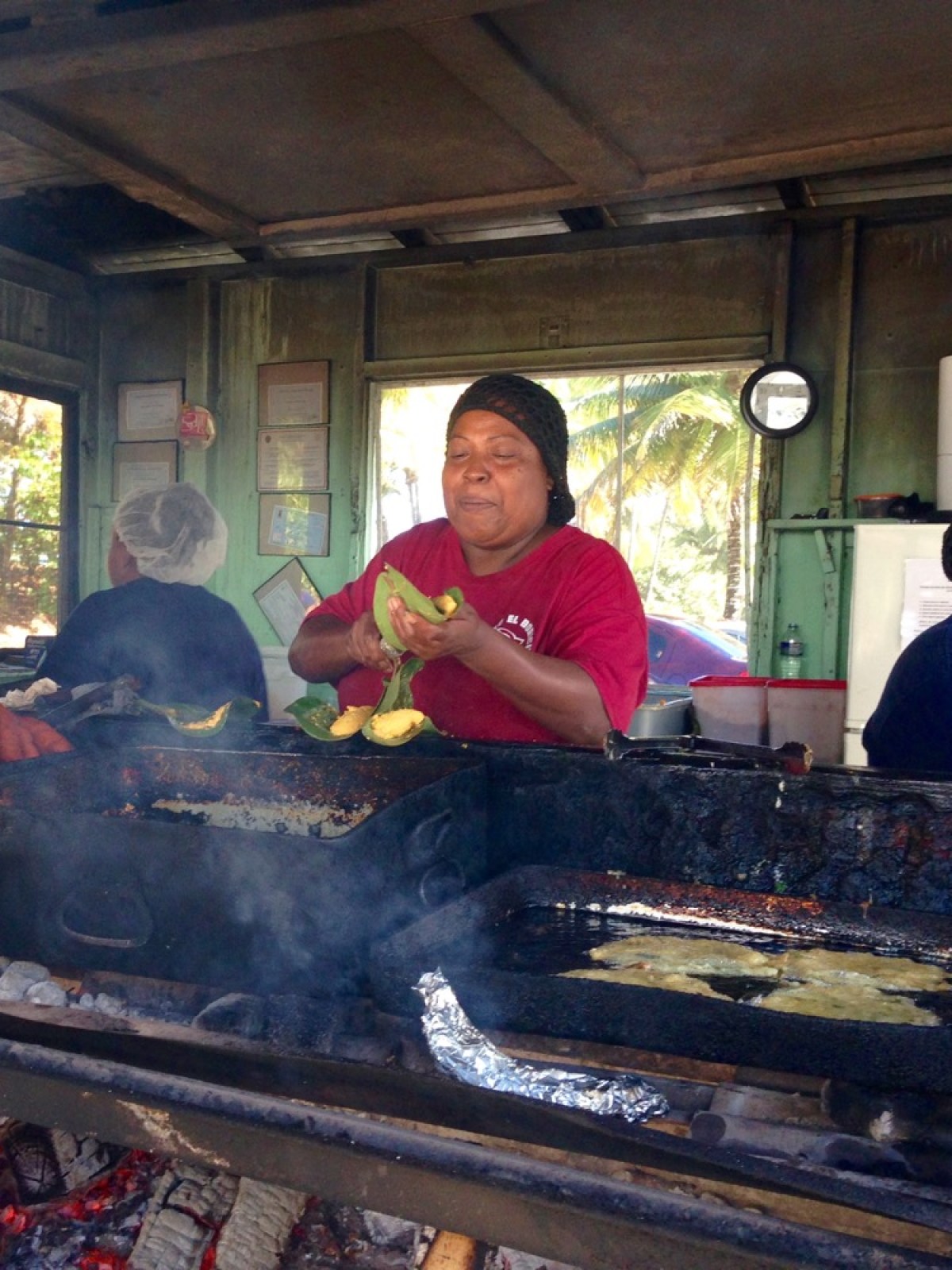 Two women cooking in an outdoor kitchen with smoke and various foods on grills.