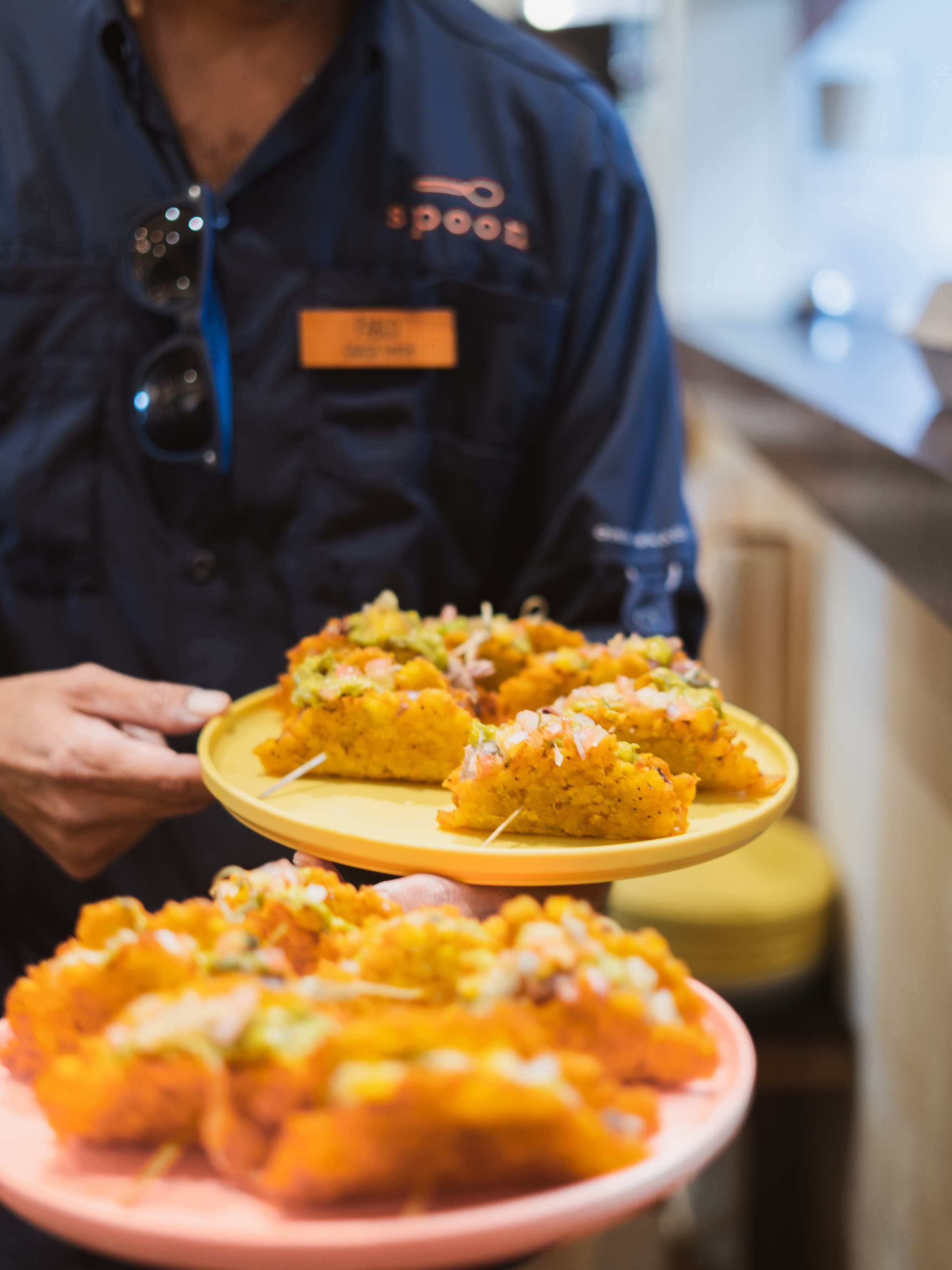Person serving plates with tacos topped with diced vegetables and sauce.