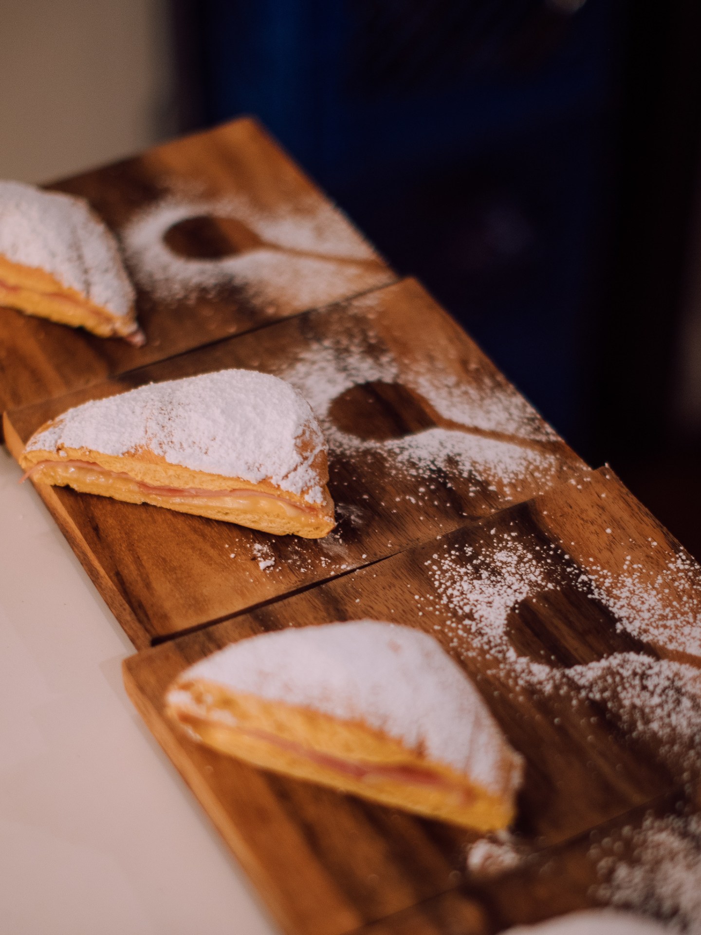 Three powdered sugar-covered pastries on wooden boards arranged in a row.