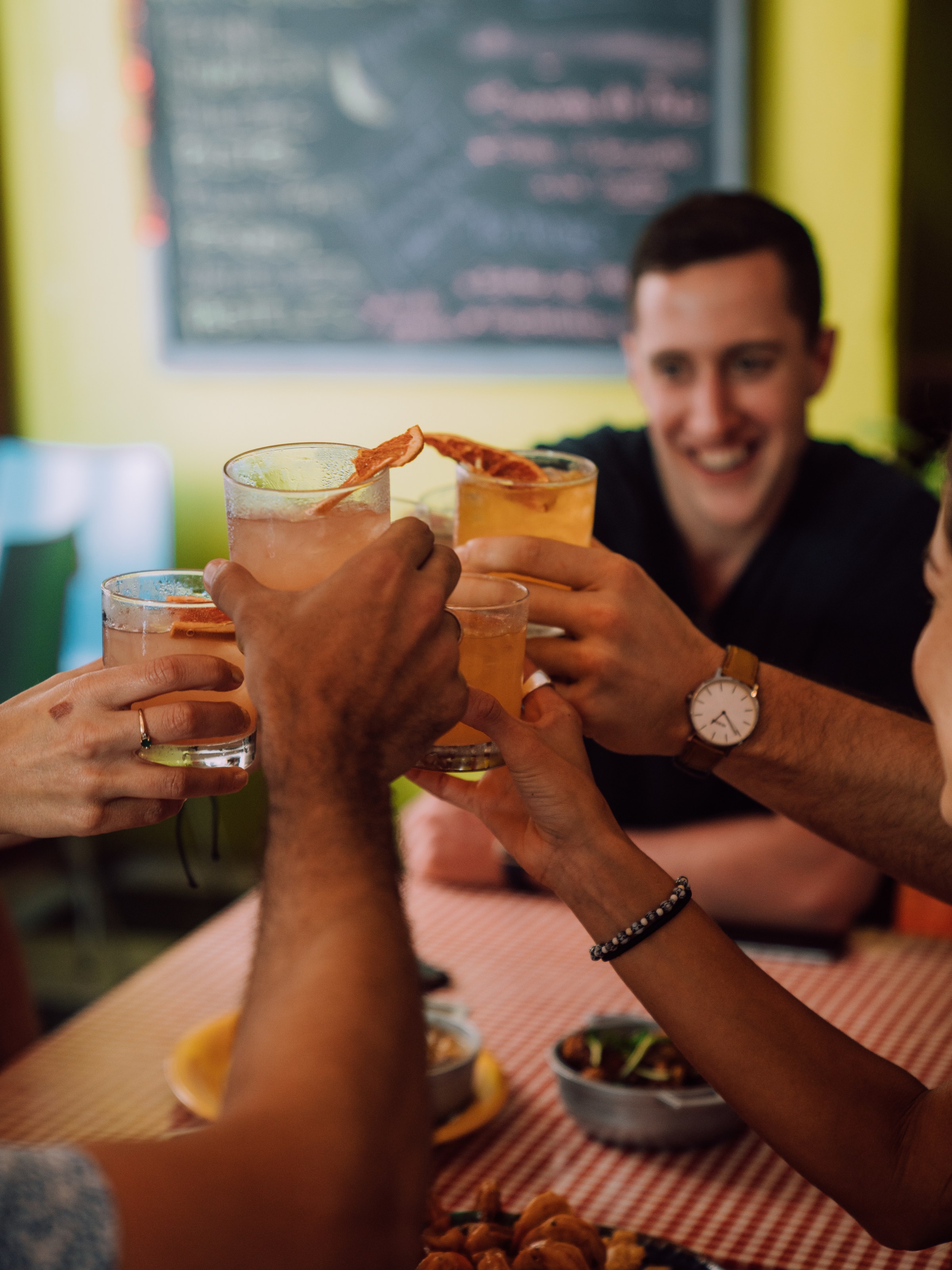 Group of friends toasting with drinks at a table in a cozy setting.