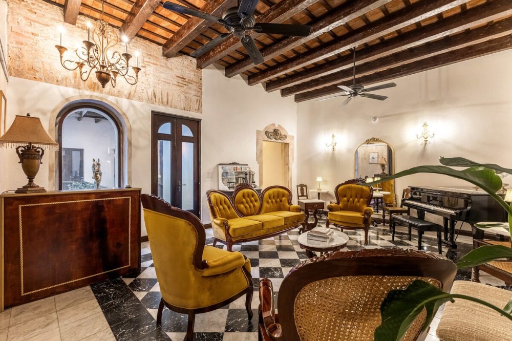 Elegant living room with vintage yellow furniture, chandeliers, and a piano on checkered floor.