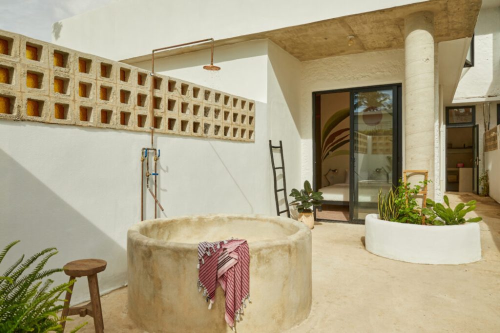 Outdoor patio with a round stone tub, towel, plants, and sliding doors to a room.