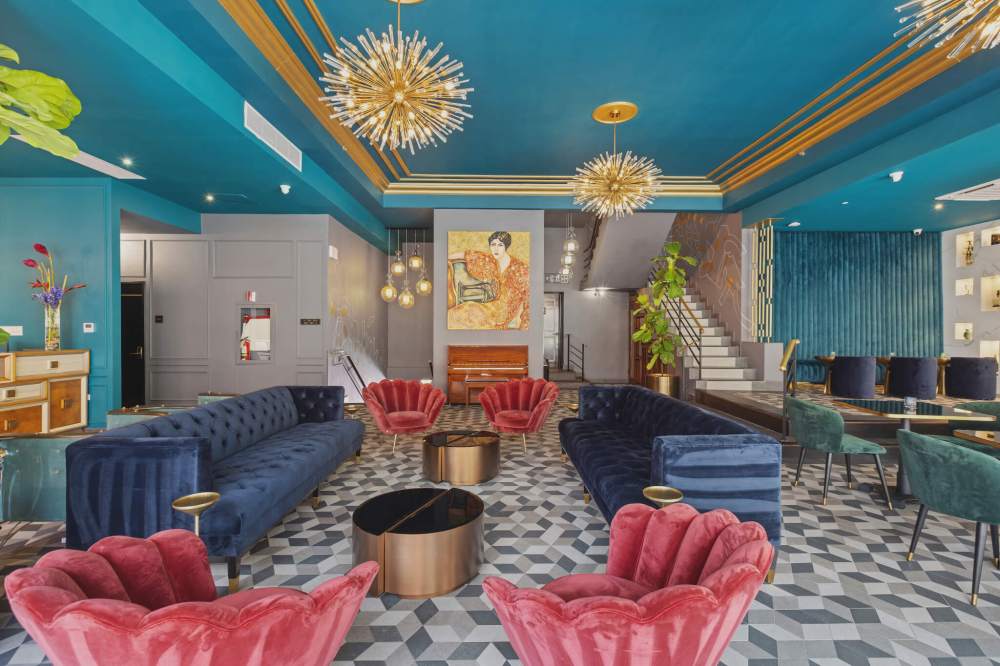 Stylish lounge with colorful chairs, blue walls, and geometric floor pattern under modern chandeliers.