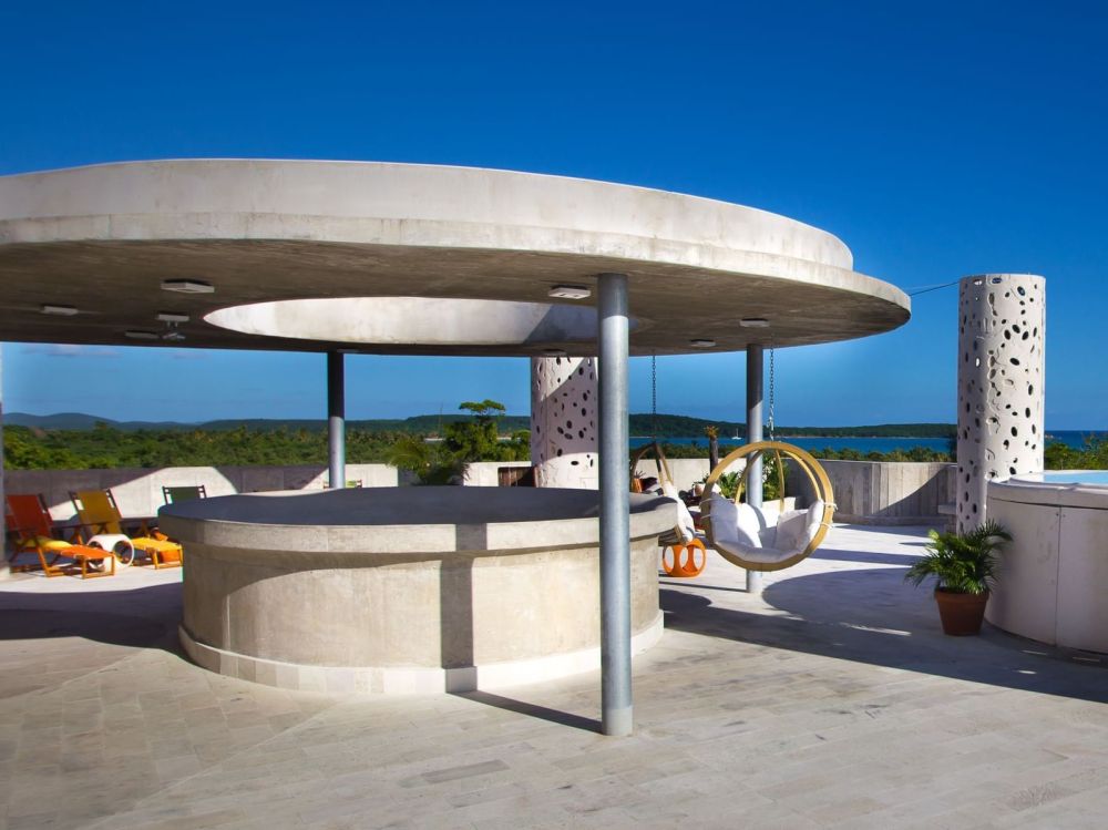 Modern rooftop terrace with circular bar, chairs, and sea view under a clear blue sky.
