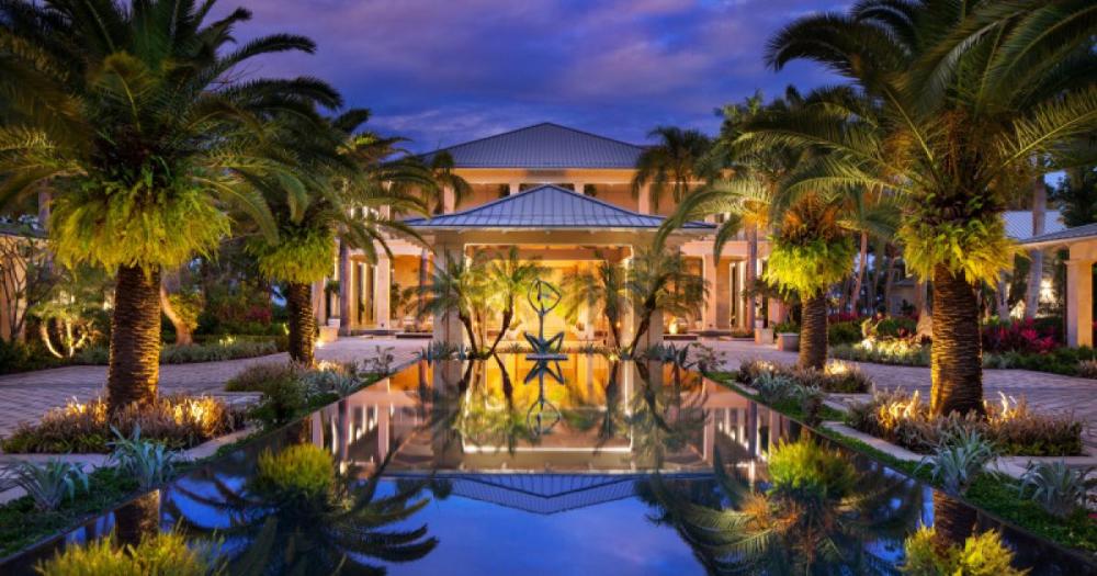 Elegant house exterior with palm trees and reflecting pool at dusk.