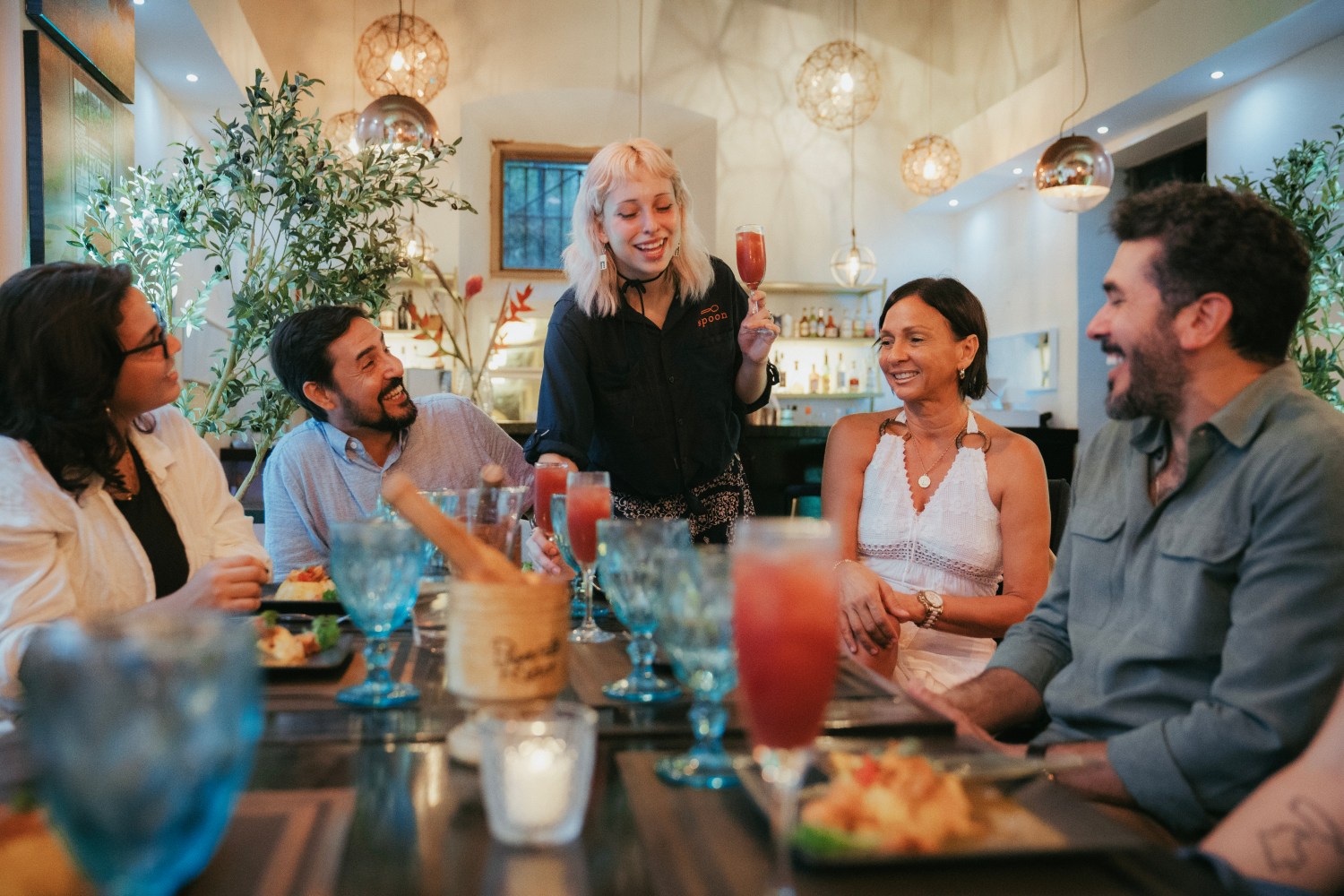 Server presenting drinks to a group of people dining together in a modern restaurant.