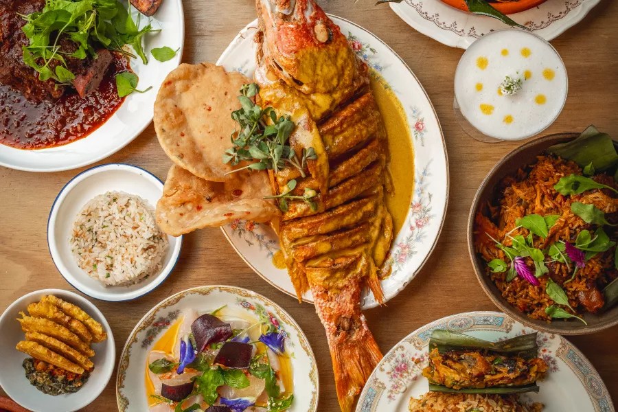 Variety of colorful dishes on a wooden table, centered around a cooked fish.