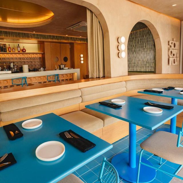 Modern restaurant interior with blue tables, beige seating, and circular wall accents.